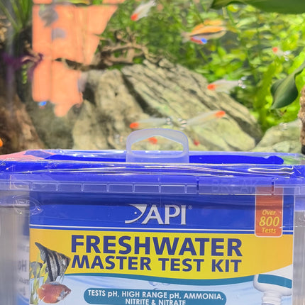 API Freshwater Master Test Kit in a clear plastic storage box with a blue lid and blue label, set against a blurred aquarium background.